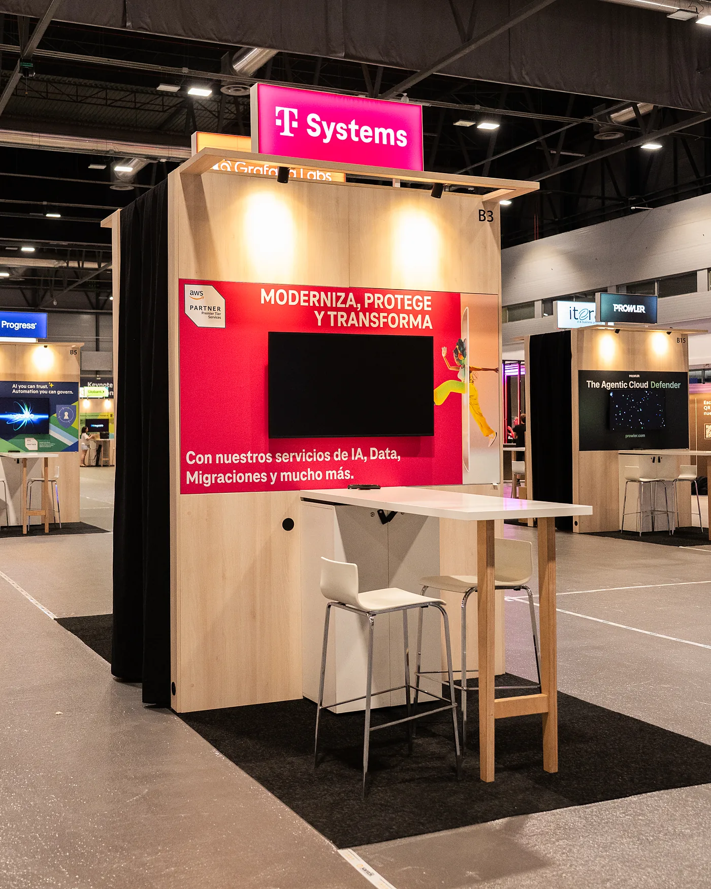 Stand van T-Systems op de beursvloer, met een magenta printwand, een scherm en een statafel met krukken