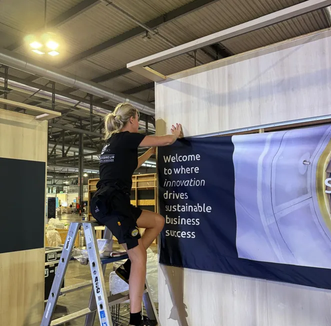 Monteur op een trap brengt een printdoek aan op de standwand