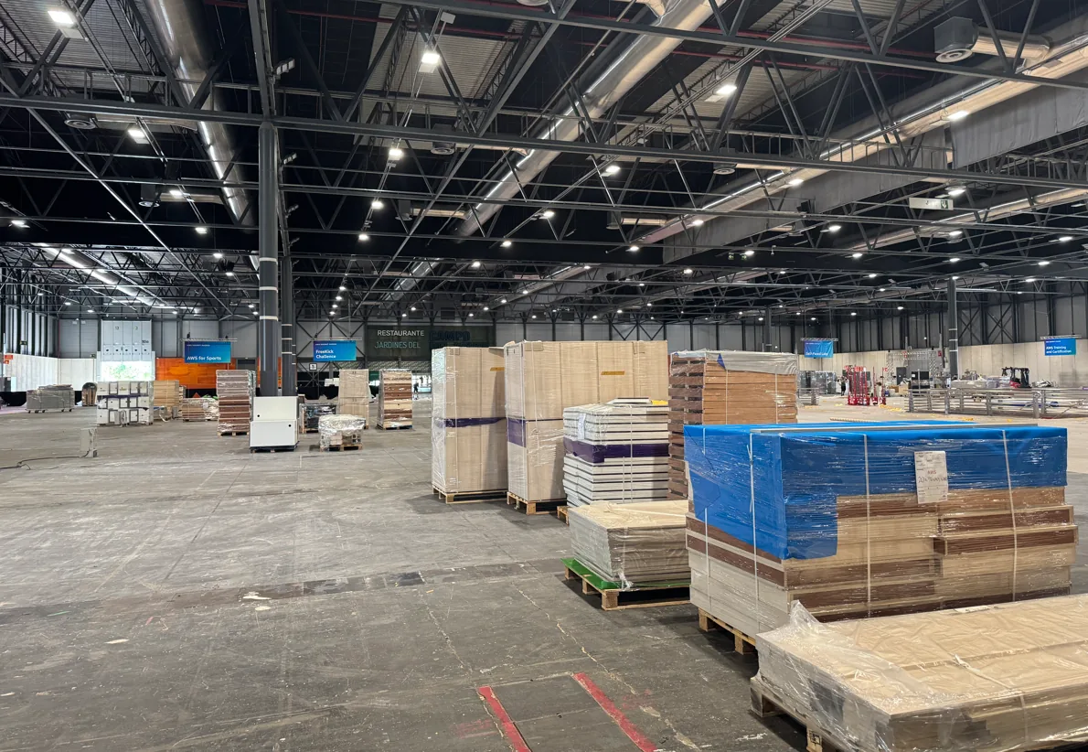 Lege beurshal met pallets vol standdelen in folie, klaar voor de opbouw