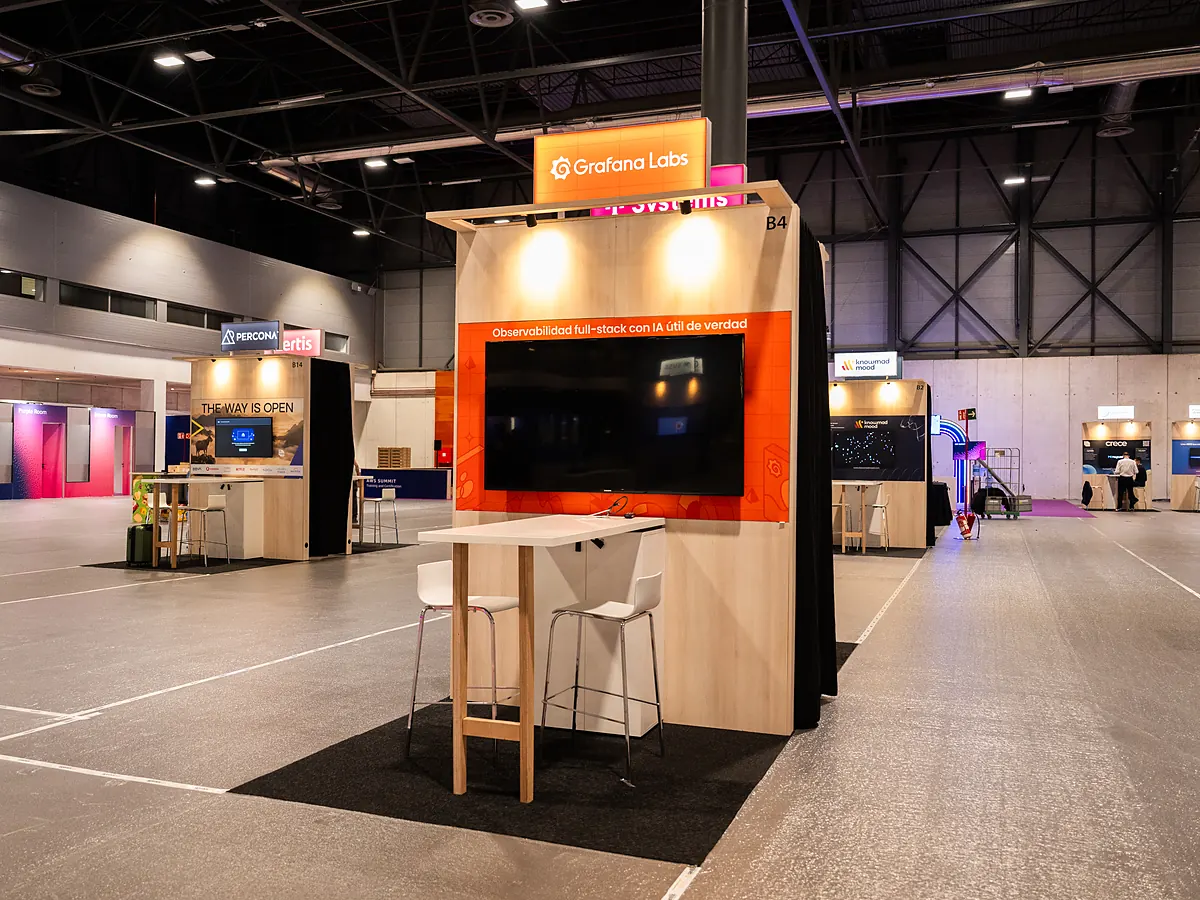 Stand van Grafana Labs met een oranje printwand, een scherm en een statafel met krukken