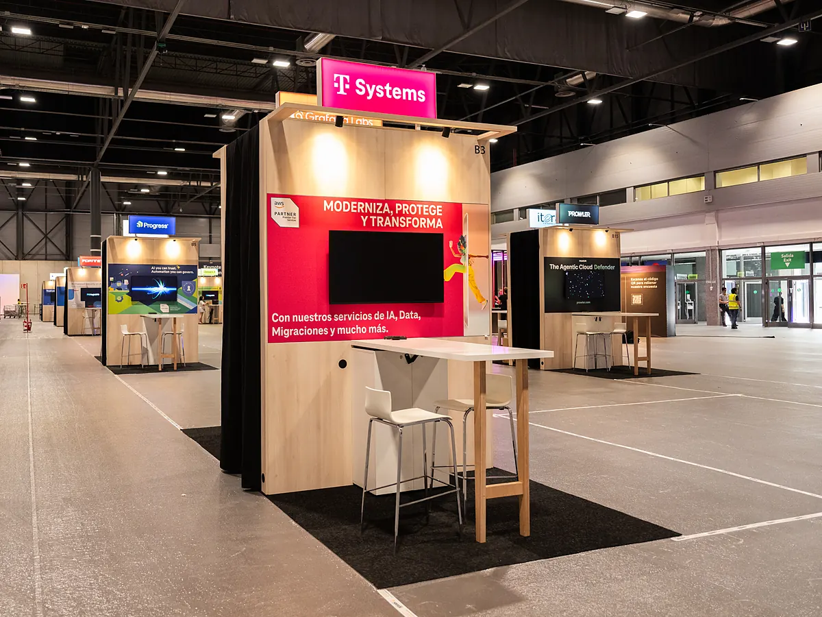 Stand van T-Systems met een magenta printwand, een scherm en een statafel met krukken