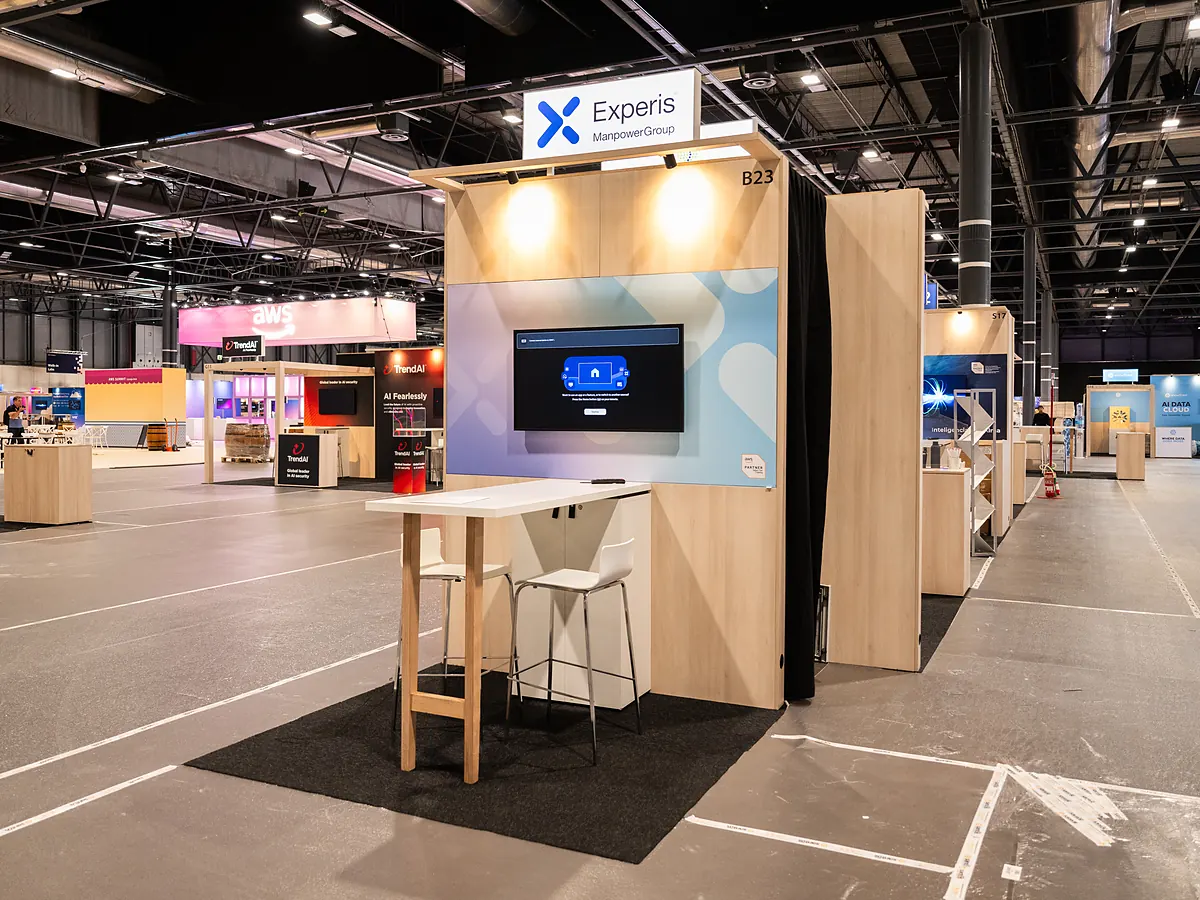 Stand van Experis met een lichtblauwe printwand, een scherm en een statafel met krukken