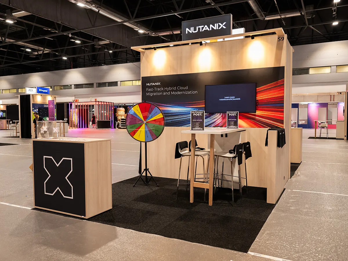 Stand van Nutanix met een donkere printwand, een scherm, een rad van fortuin en een balie met logo
