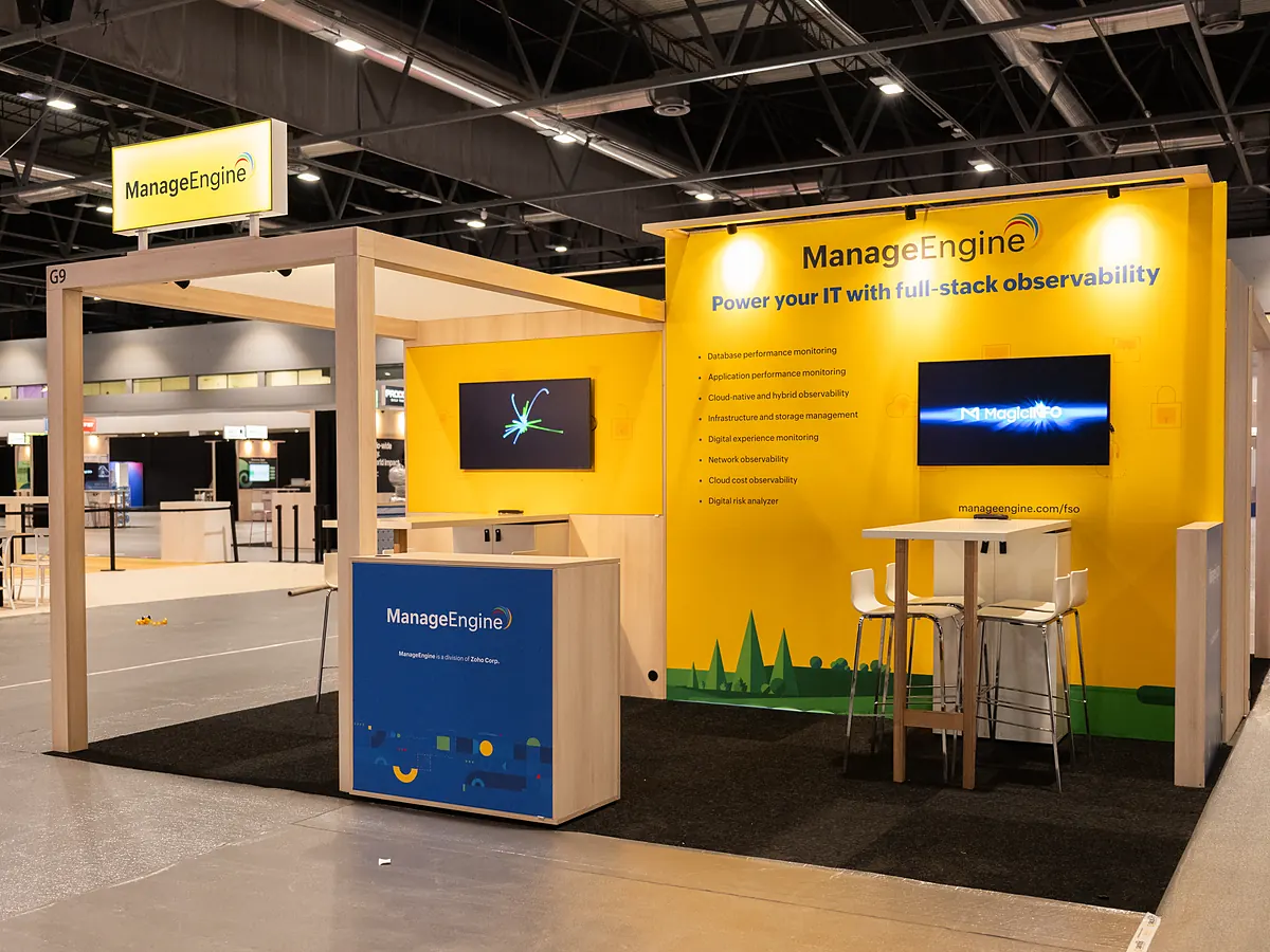 Stand van ManageEngine met een gele full color printwand, twee schermen en een balie met print