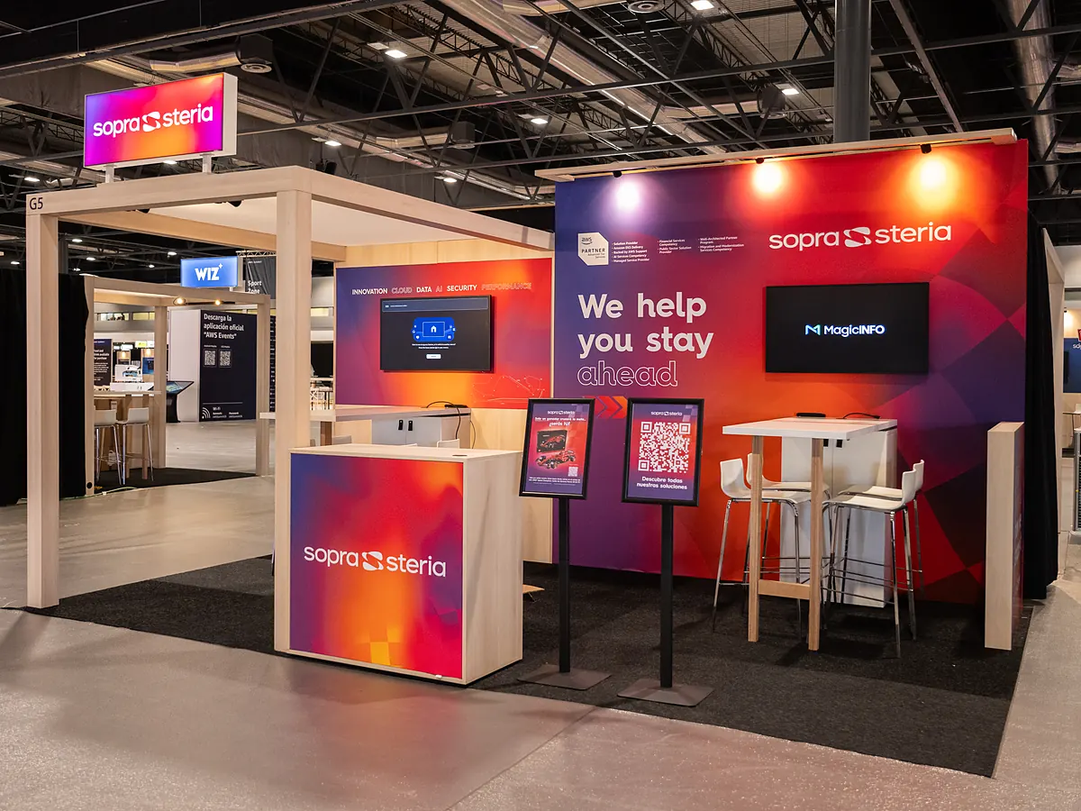 Stand van Sopra Steria met een printwand in rood en paars, een scherm, een balie met logo en een statafel met krukken