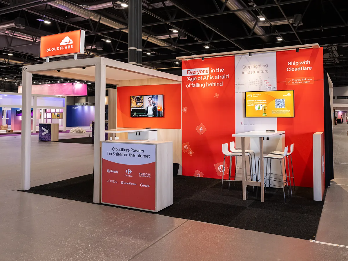 Stand van Cloudflare met oranje printwand, verlichte logokast boven het portaal en een balie met partnerlogo's