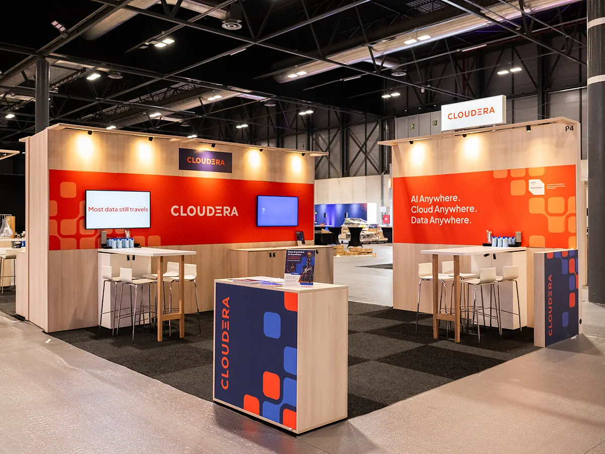 Stand van Cloudera met oranje printwanden, een scherm en een balie met logo